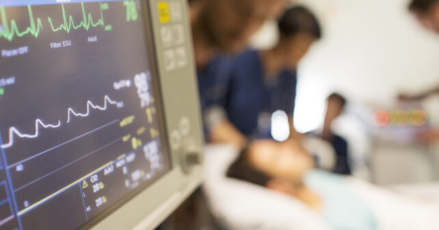 Heart rate monitor, patient and doctors in background in intensive care unit